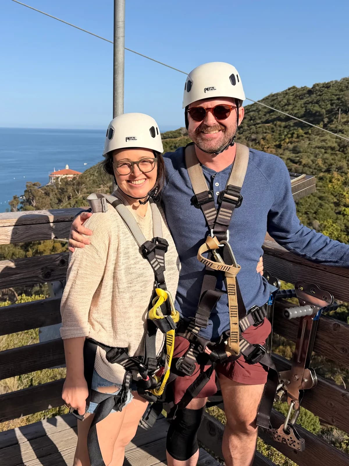 Connie and Brian smiling outdoors in helmets and climbing harnesses.