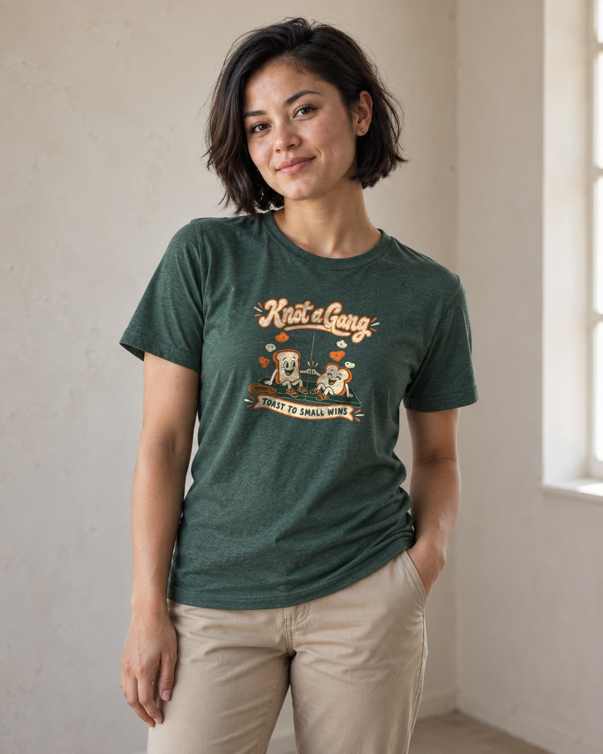 A woman wearing the Heather Forest Green Toast to Small Wins T-shirt in natural studio light.