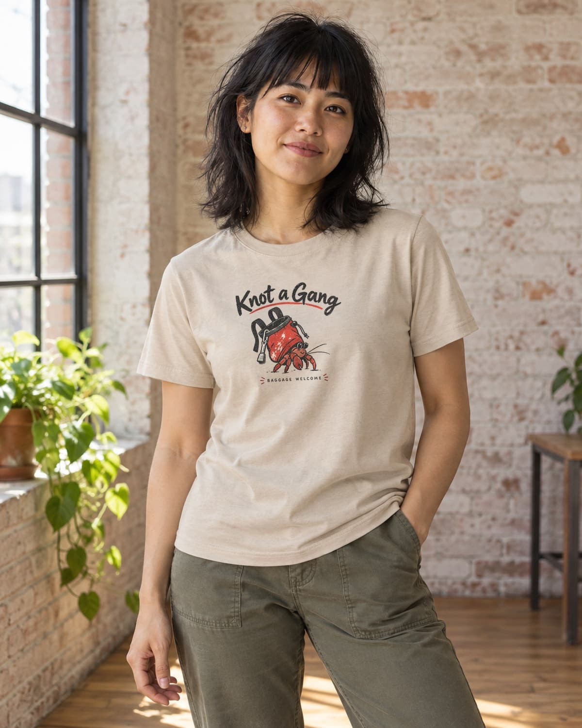 A woman wearing the Sand Baggage Welcome T-shirt in natural studio light.