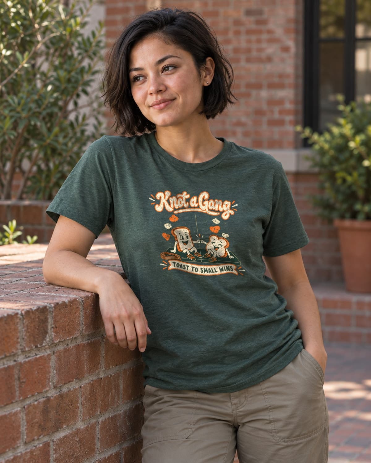 A woman wearing the Heather Forest Green Toast to Small Wins T-shirt in a relaxed lifestyle setting.
